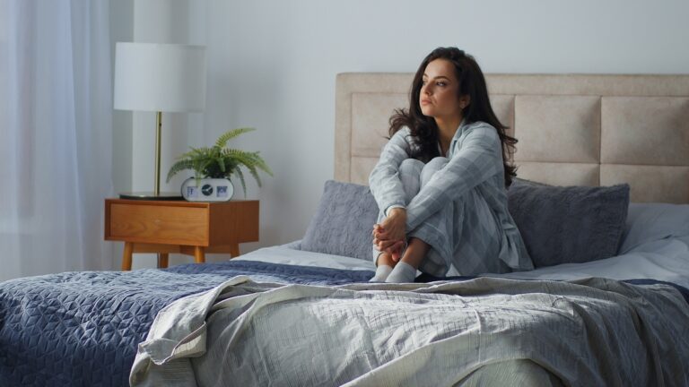 Woman sitting alone on bed looking distant, wondering if it is sadness or depression