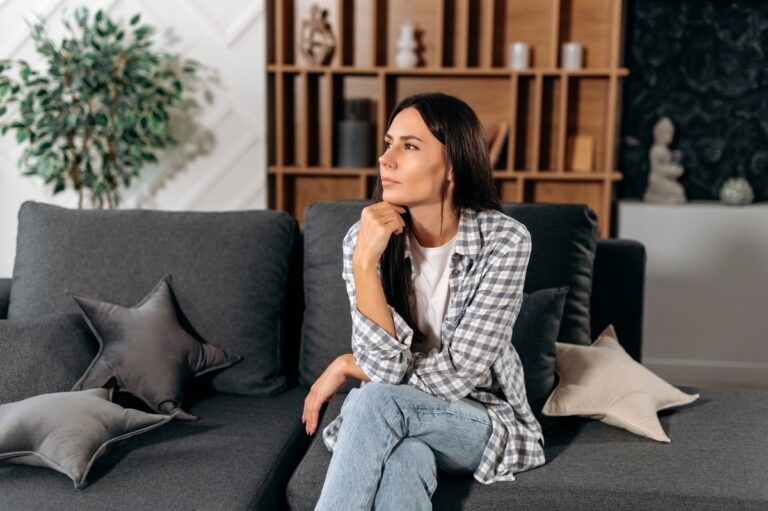 Adult woman sitting thoughtfully on a couch representing the experience of living with both ADHD and depression