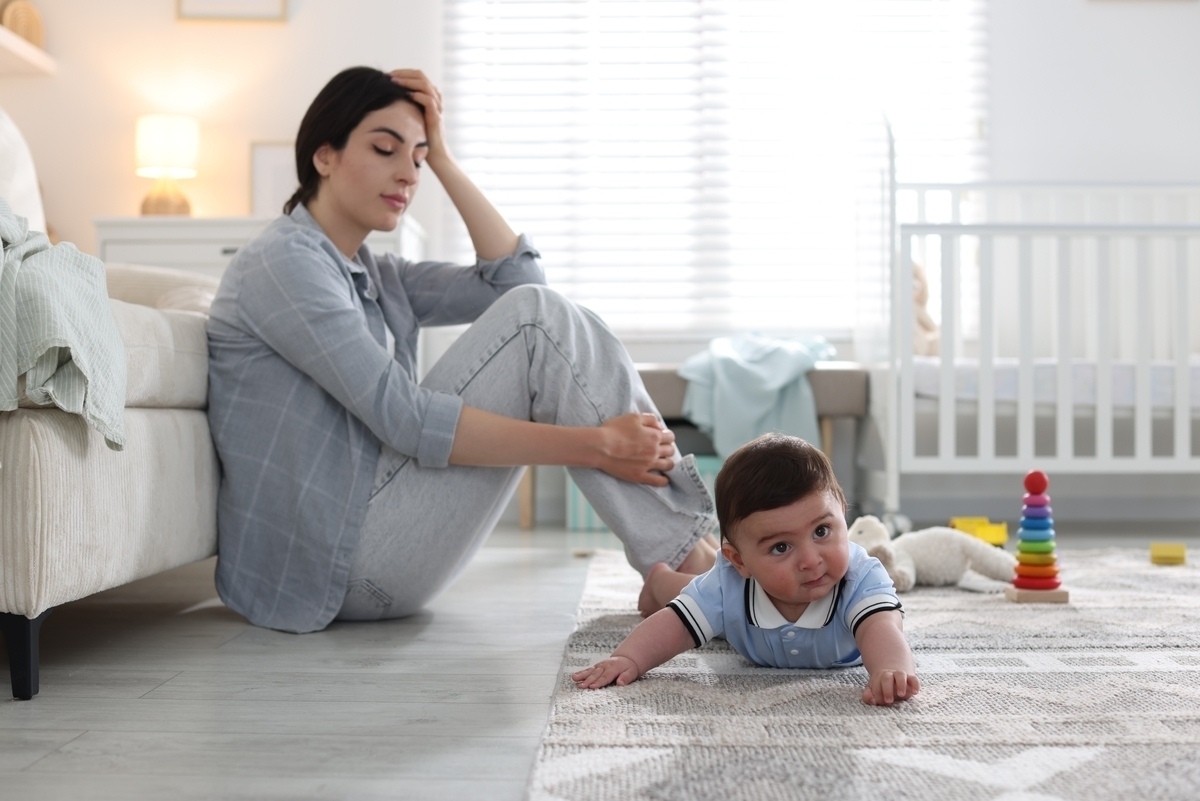 Exhausted mother sitting on the floor beside her baby representing the emotional experience of postpartum depression