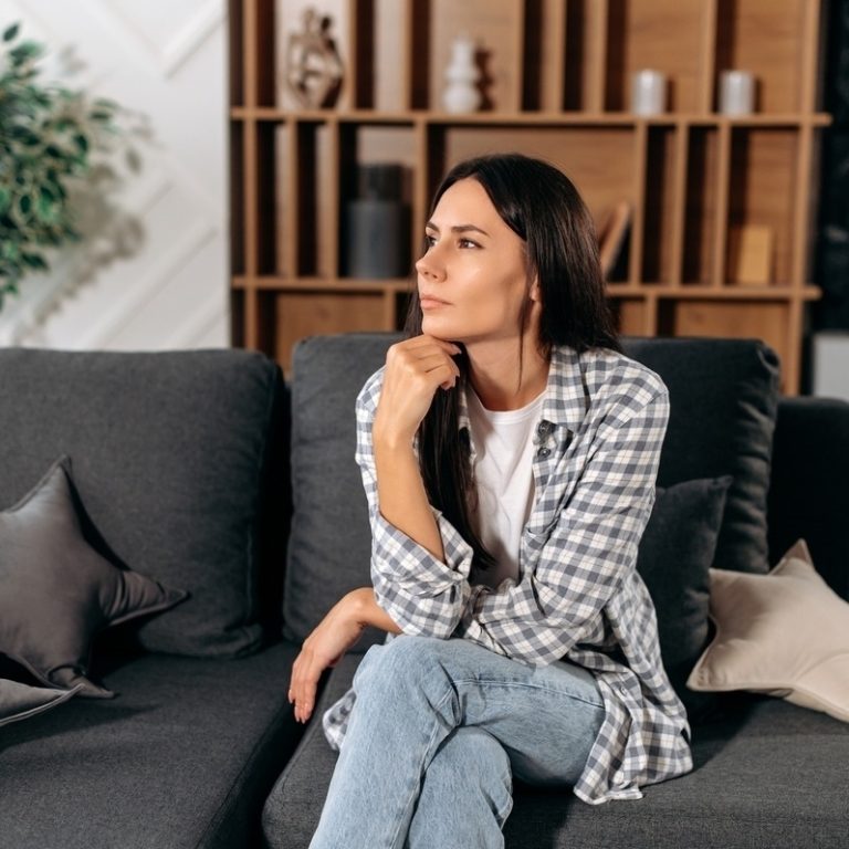 Adult woman sitting thoughtfully on a couch representing the experience of living with both ADHD and depression