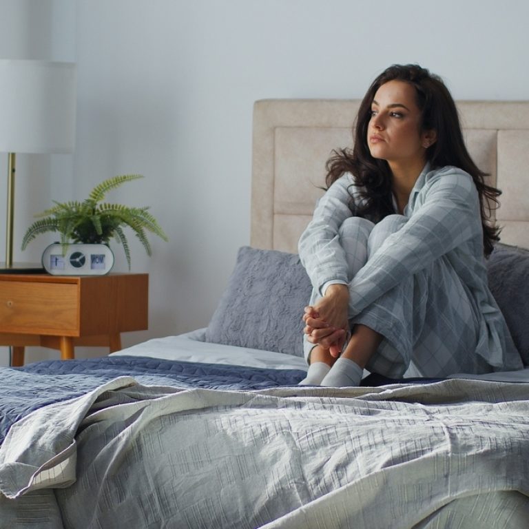 Woman sitting alone on bed looking distant, wondering if it is sadness or depression